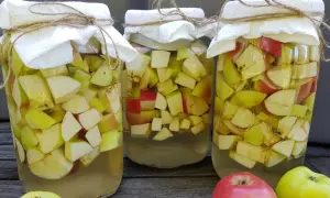 Trzy słoje z jabłkami, przygotowywane do produkcji octu. Słoje przykryte są papierem i sznurkiem.