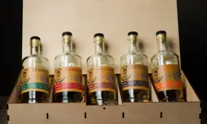 Pięć butelek nalewek ziemniaczanych w drewnianej skrzynce: leśna, jesienna, orzechowa, czekoladowa i pomarańczowa.