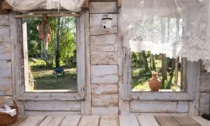 Widok z okna na podwórko, gdzie widać stare narzędzia rolnicze i drzewa. W koszyku leżą białe tkaniny, a na parapecie gliniana waza. To miejsce, gdzie można poczuć zysk z kurnika.