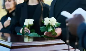 Pogrzeb, trumna, białe róże, żałobnicy w czarnych ubraniach.