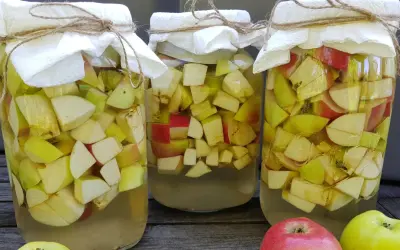 Trzy słoje z jabłkami, przygotowywane do produkcji octu. Słoje przykryte są papierem i sznurkiem.