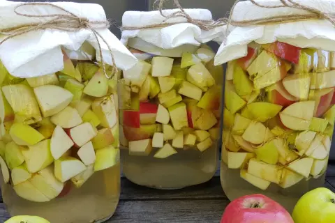 Trzy słoje z jabłkami, przygotowywane do produkcji octu. Słoje przykryte są papierem i sznurkiem.