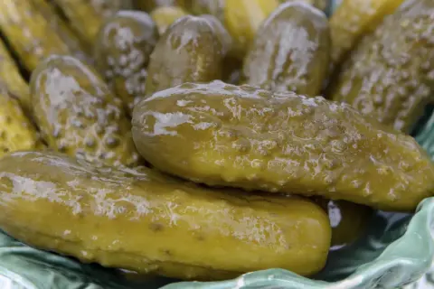 Kosz pełen soczystych, zielonych ogórków kiszonych, które wyglądają na puste w środku, gotowe do chrupania.