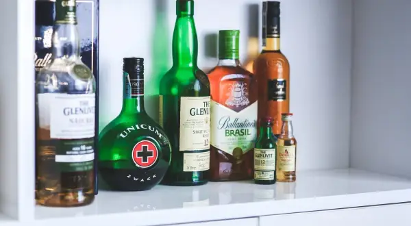 Rząd butelek z alkoholami, w tym Unicum i różne whisky, jakby zapomniane nalewki czekające na degustację.