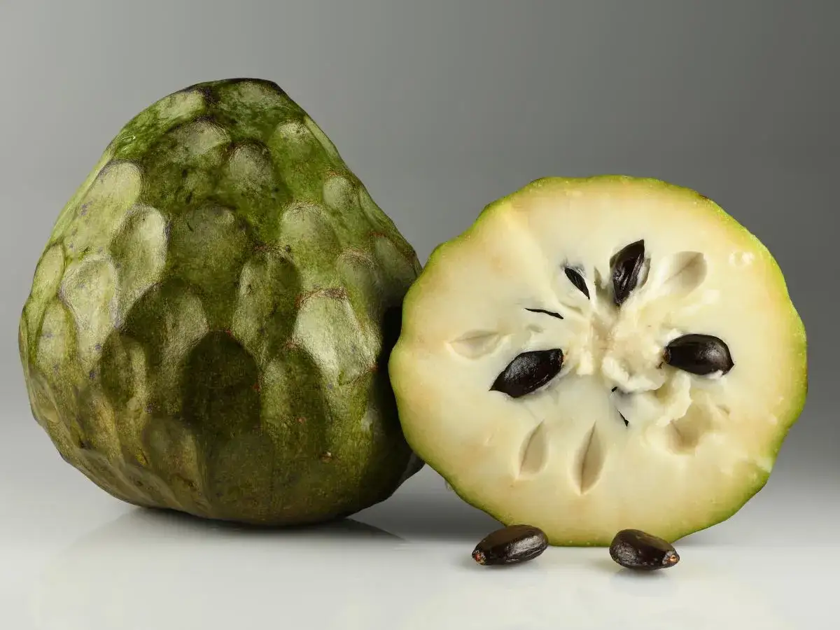 Zielona cherimoya owoc, przekrojona na pół, ukazuje kremowe wnętrze z czarnymi pestkami.