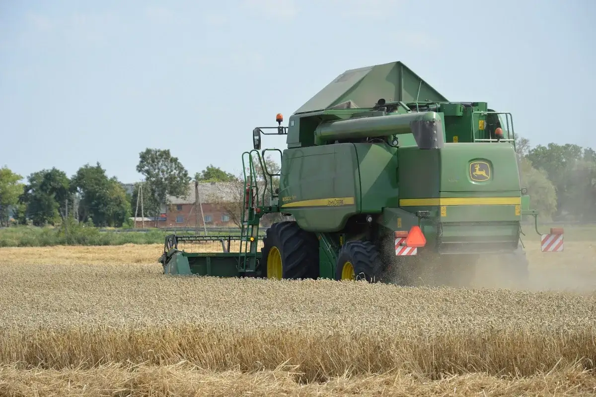 Kombajn John Deere zbiera pszenicę na polu, pokazując potencjał, ile Polska produkuje pszenicy.