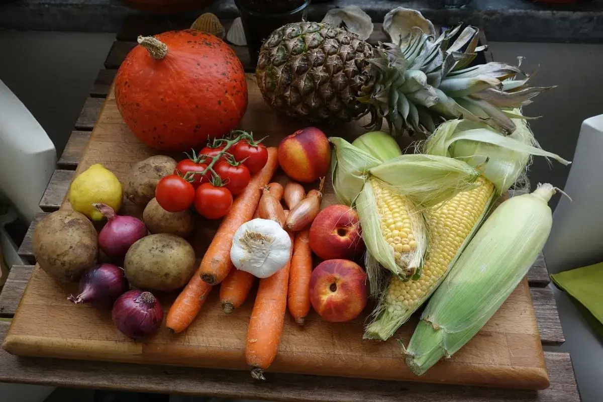 Różnica między owocem a warzywem? Na desce dynia, ananas, pomidory, kukurydza, ziemniaki, marchewki, czosnek, cebula, cytryna i nektarynki.