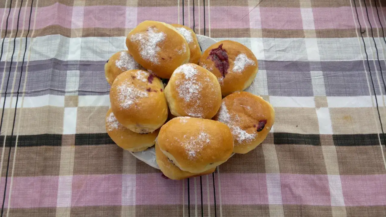 Stos świeżo upieczonych jagodzianek domowych, posypanych cukrem pudrem, czeka na swój przepis.