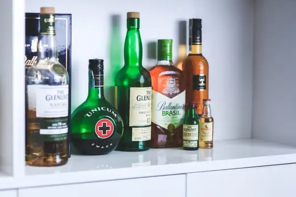 Rząd butelek z alkoholami, w tym Unicum i różne whisky, jakby zapomniane nalewki czekające na degustację.